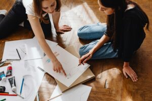 Two young women collaborating on fashion designs, sharing ideas and sketches.
